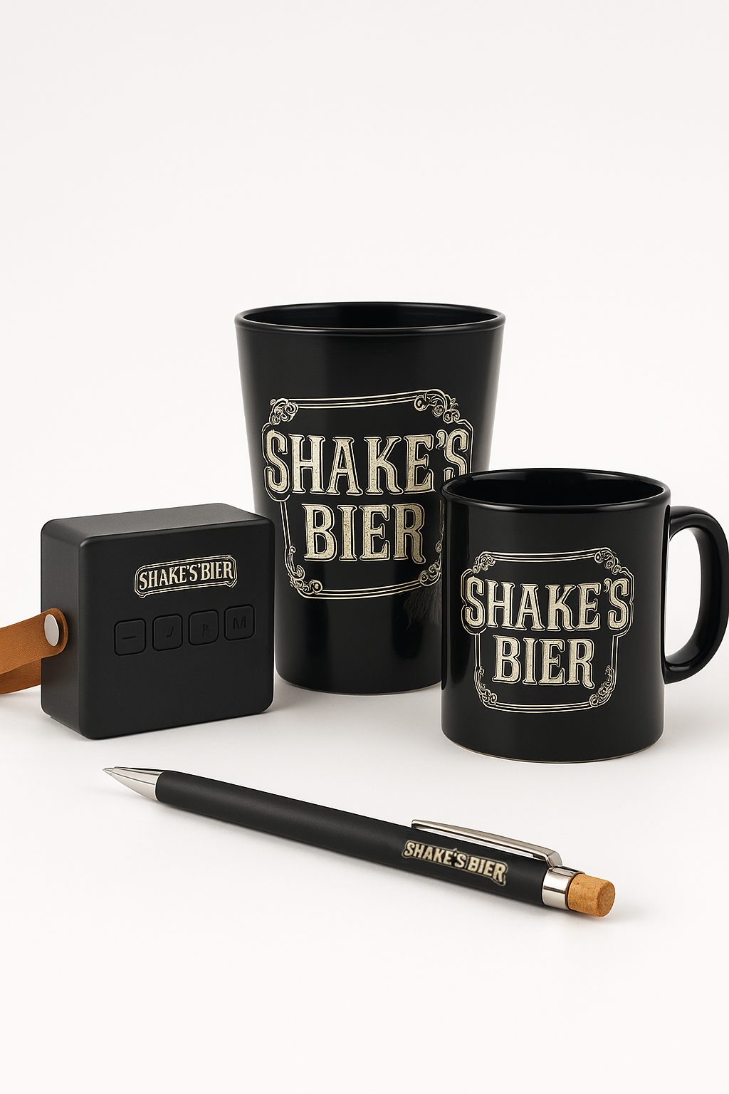 Ensemble de goodies personnalisés “Shake’s Bier” comprenant un gobelet, une tasse, une enceinte portable et un stylo, présentés sur fond clair.