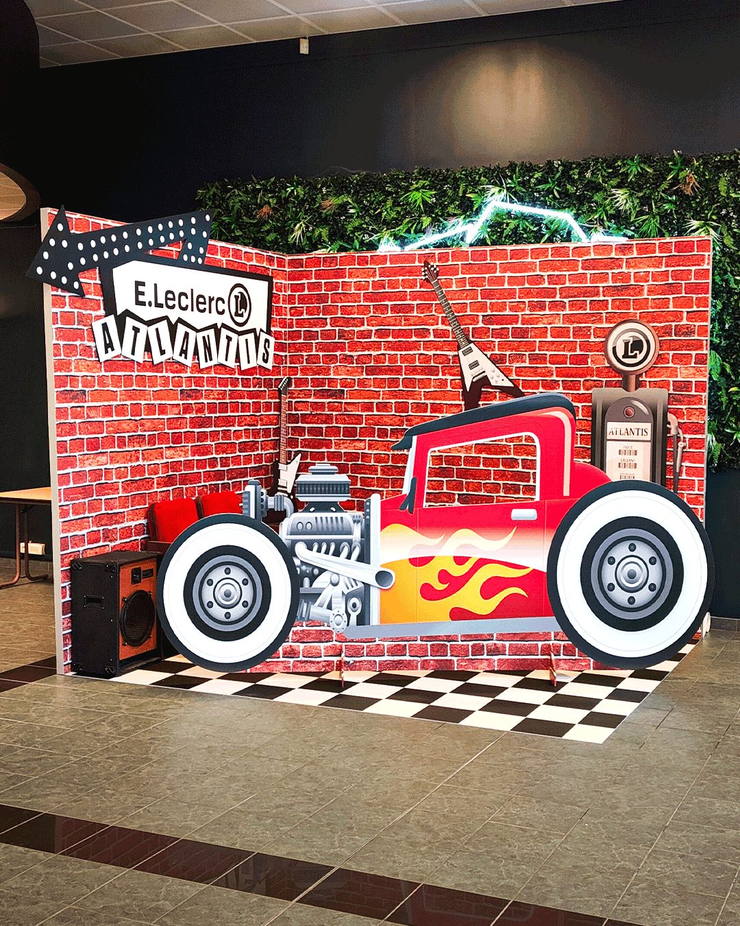 Décor événementiel avec mur brique, voiture hot rod, guitare et signalétique personnalisée “E.Leclerc Atlantis”, installé en intérieur.